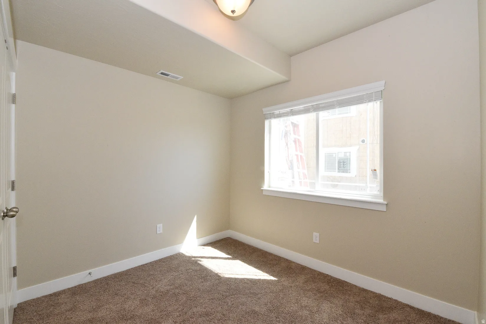 Neutral-toned room featuring a large window with horizontal blinds, providing natural illumination