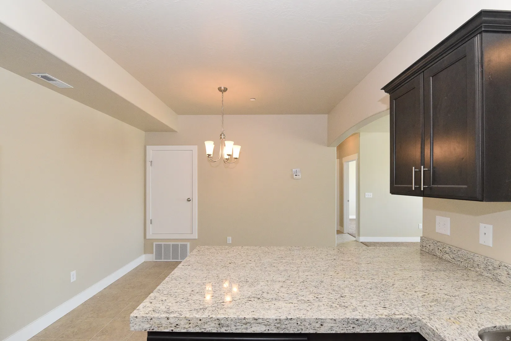 Spacious kitchen area featuring an expansive stone-finish countertop, dark wood-finish upper cabinetry with brushed nickel hardware, and tile flooring