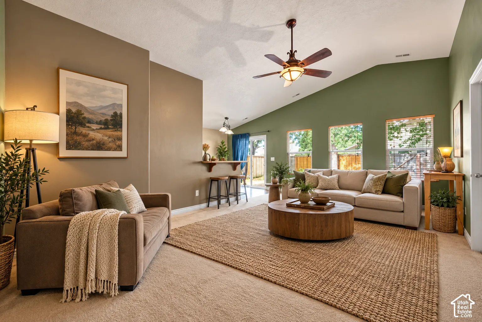 Living area featuring vaulted ceilings, a ceiling fan with integrated lighting, multiple windows, and a built-in breakfast bar. Virtually Staged.
