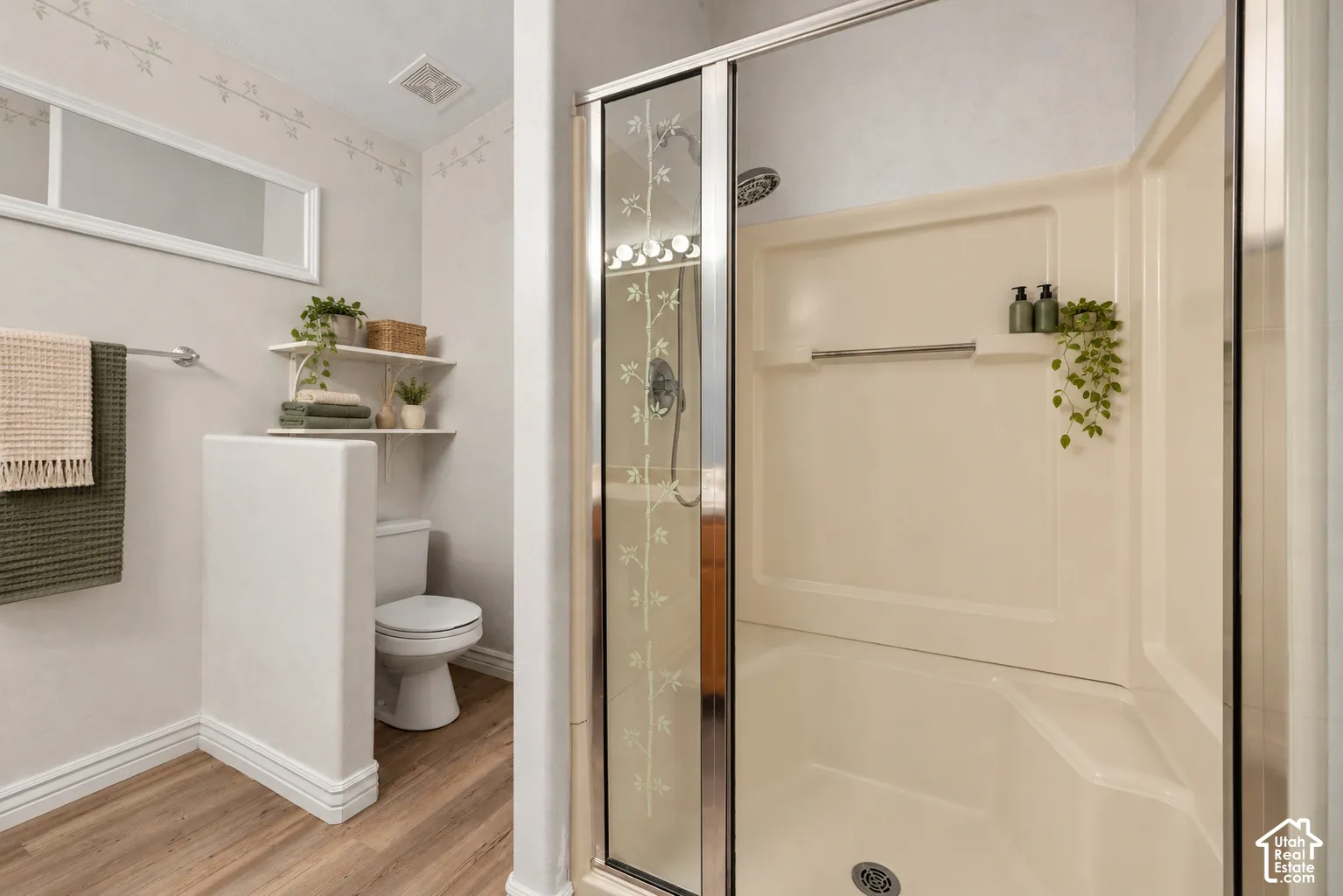 Primary Suite Bathroom featuring a walk-in shower with integrated seating, chrome hardware, etched glass enclosure, wood-finish flooring, and a partial privacy wall. Virtually Staged.