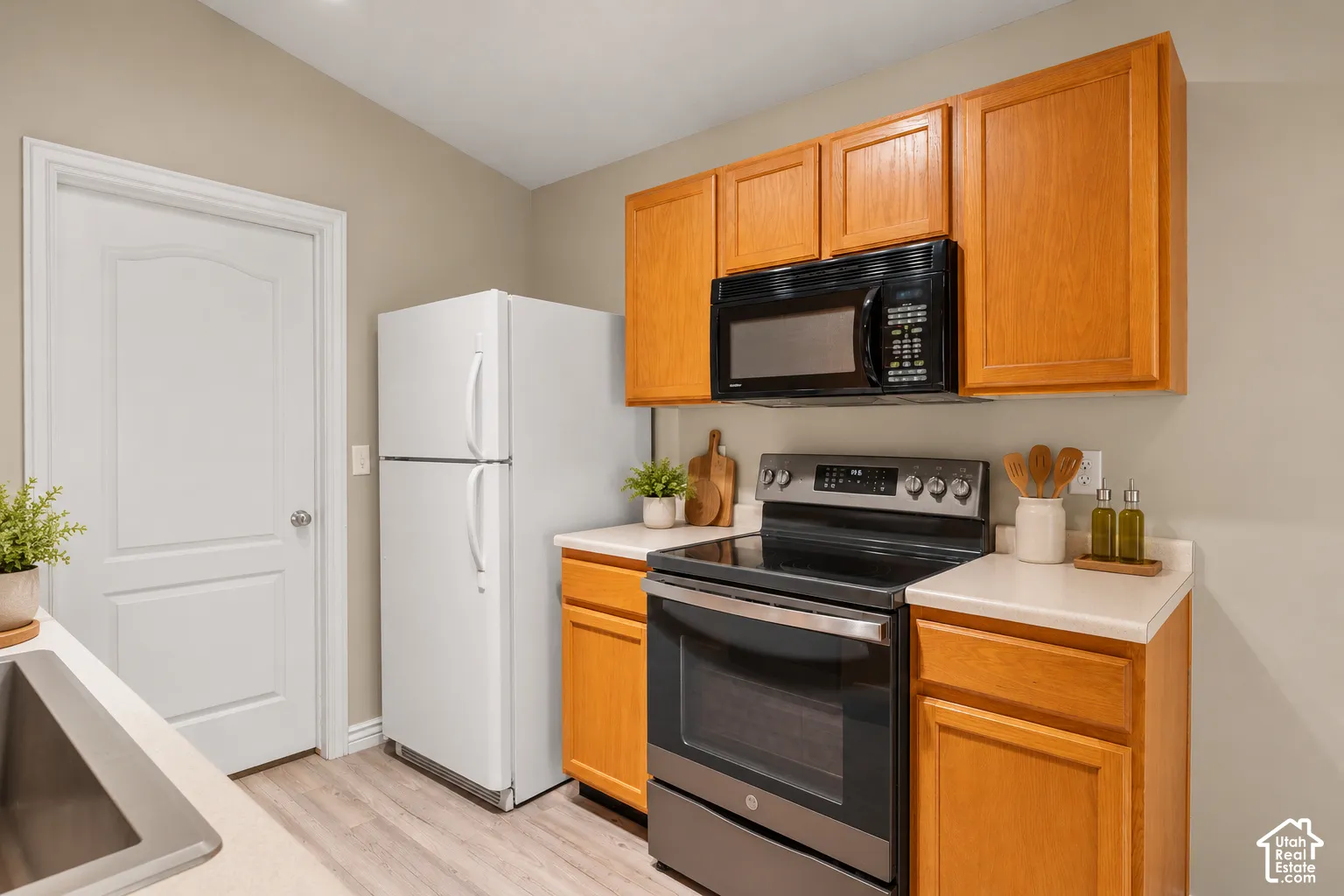 Kitchen area featuring light-tone wood cabinetry, solid-surface countertops, built-in black microwave, and stainless steel freestanding range. Virtually Staged.