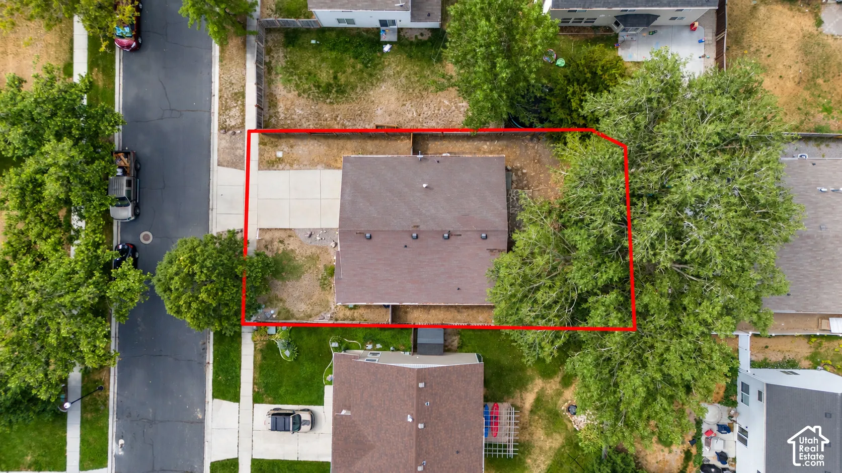 Aerial view of residential lot featuring a concrete driveway, multi-faceted roofline, and mature trees