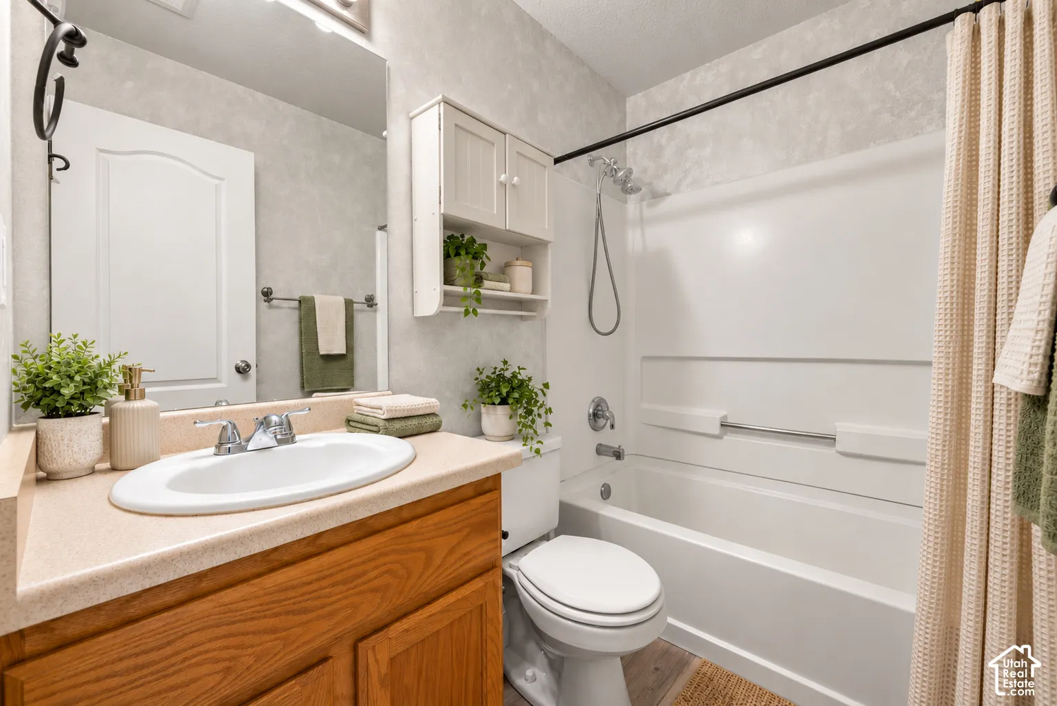 Bathroom featuring a wood-finish vanity with a solid-surface countertop and integrated oval sink, a wall-mounted storage cabinet, and a tub-shower combination with a hand-held showerhead. Virtually Staged.