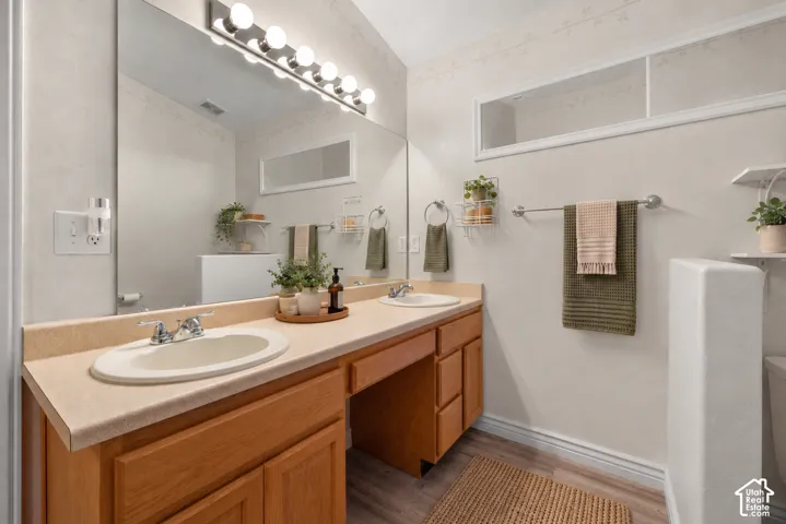 Primary Suite Bathroom with dual-sink vanity with wood-finish cabinetry, solid-surface countertop, full-width wall mirror, and integrated lighting. Virtually Staged.
