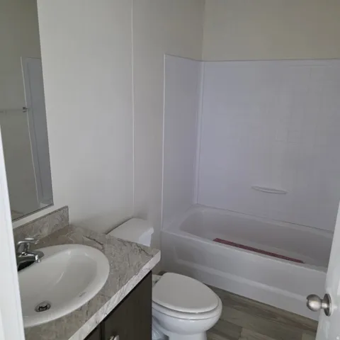 Bathroom featuring a white bathtub with a wall surround, a toilet, a vanity with a counter and integrated sink, and wood-finish flooring