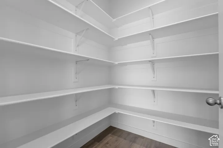 Walk-in pantry featuring white shelving, a light wood-finish floor, and a brushed nickel doorknob