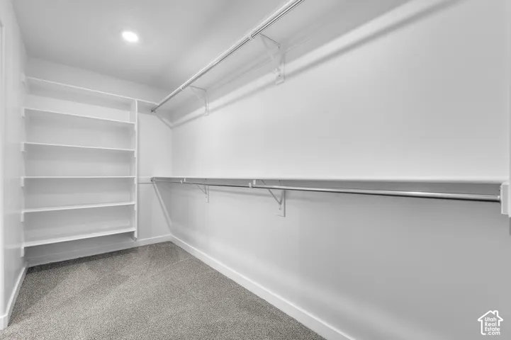Spacious closet featuring built-in shelving, dual hanging rods, recessed ceiling lighting, and grey carpet flooring
