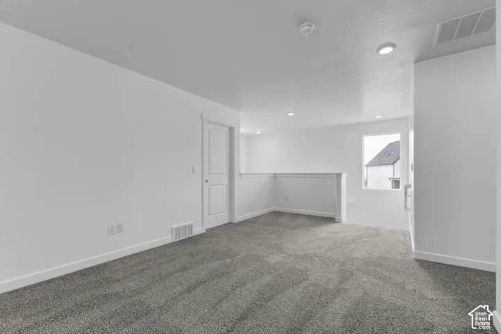 Carpeted upper-level landing featuring a white painted railing, recessed lighting, and a white interior door