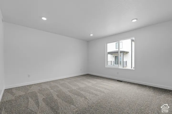 Spacious room featuring a large window, recessed lighting, white walls, white baseboards, and patterned carpeting