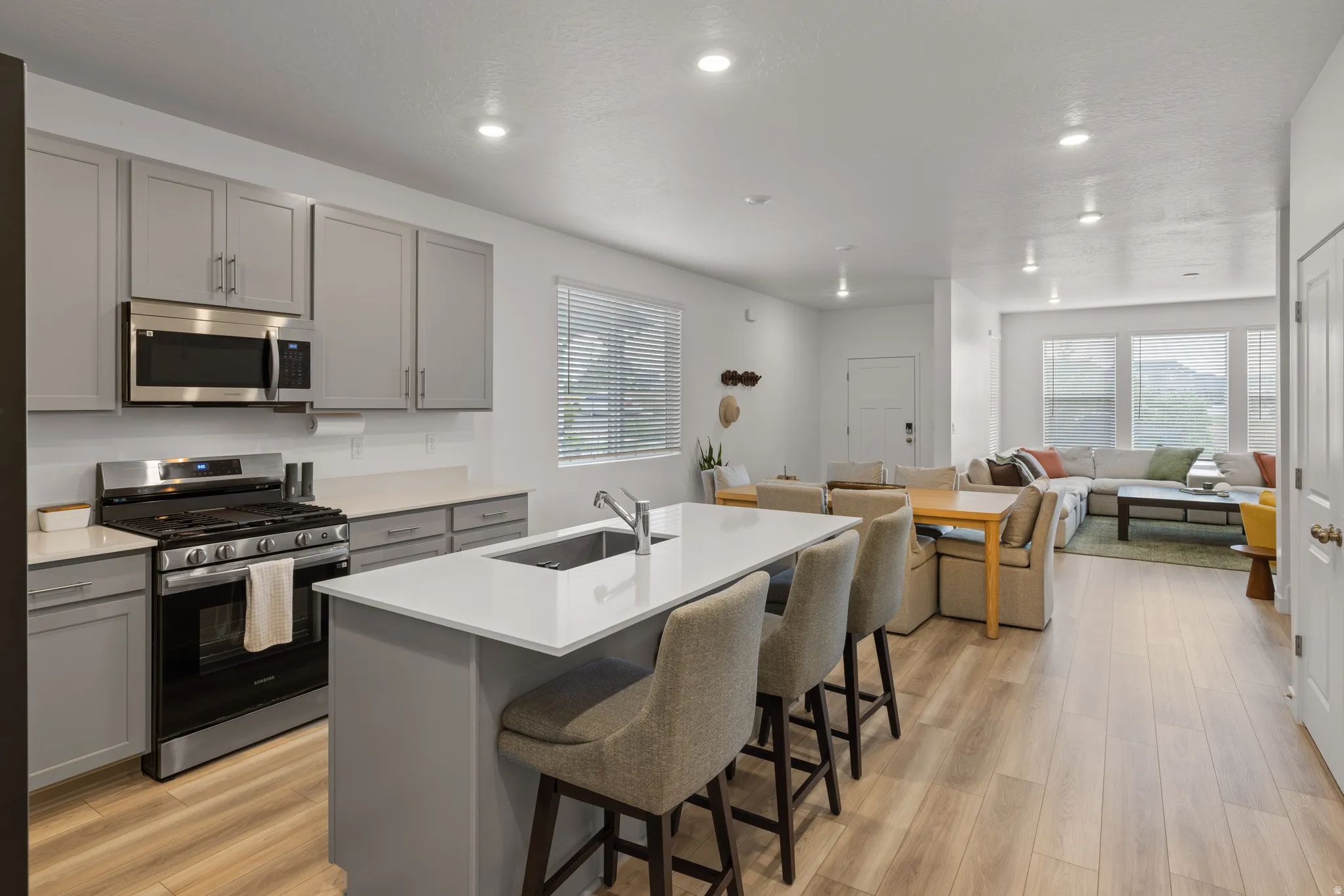 Open-concept kitchen featuring an eat-at island with a stainless steel sink, stainless steel appliances, light gray cabinetry, and wood-finish flooring