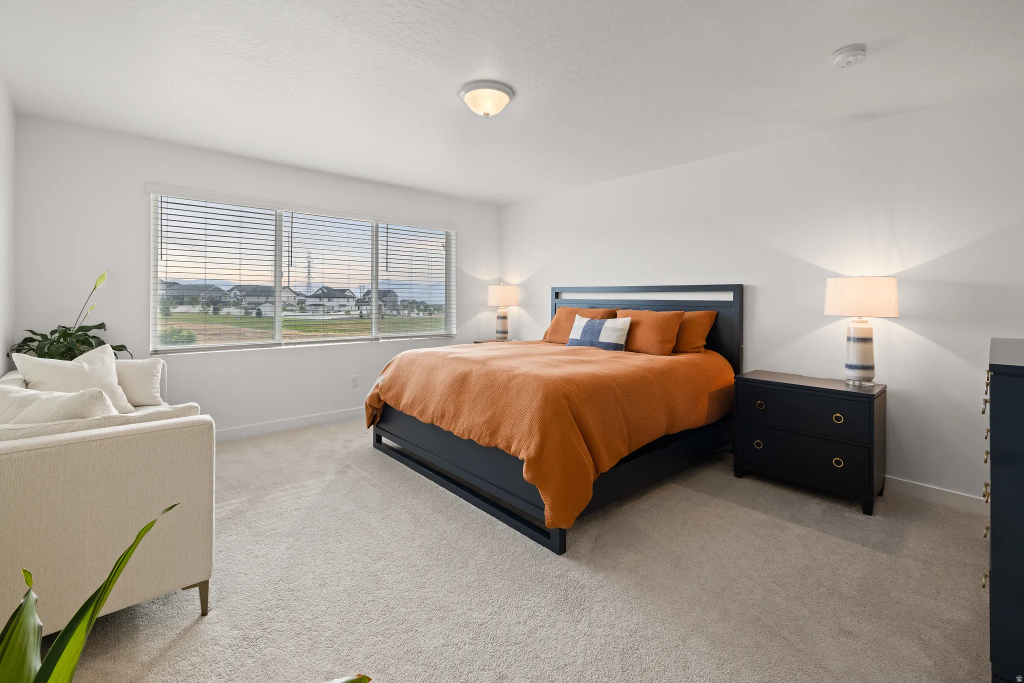 Expansive master bedroom featuring a wide window with horizontal blinds, neutral carpet flooring, and recessed ceiling light fixtures