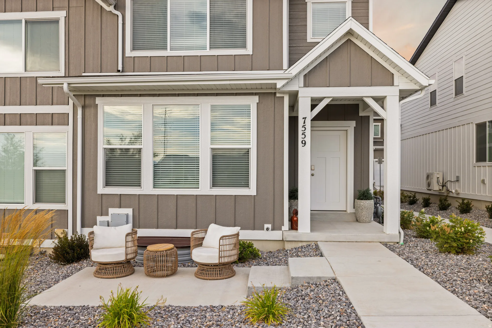 Modern townhome exterior featuring vertical and horizontal siding, a covered entry with white columns and gable, a white front door, and a concrete pathway