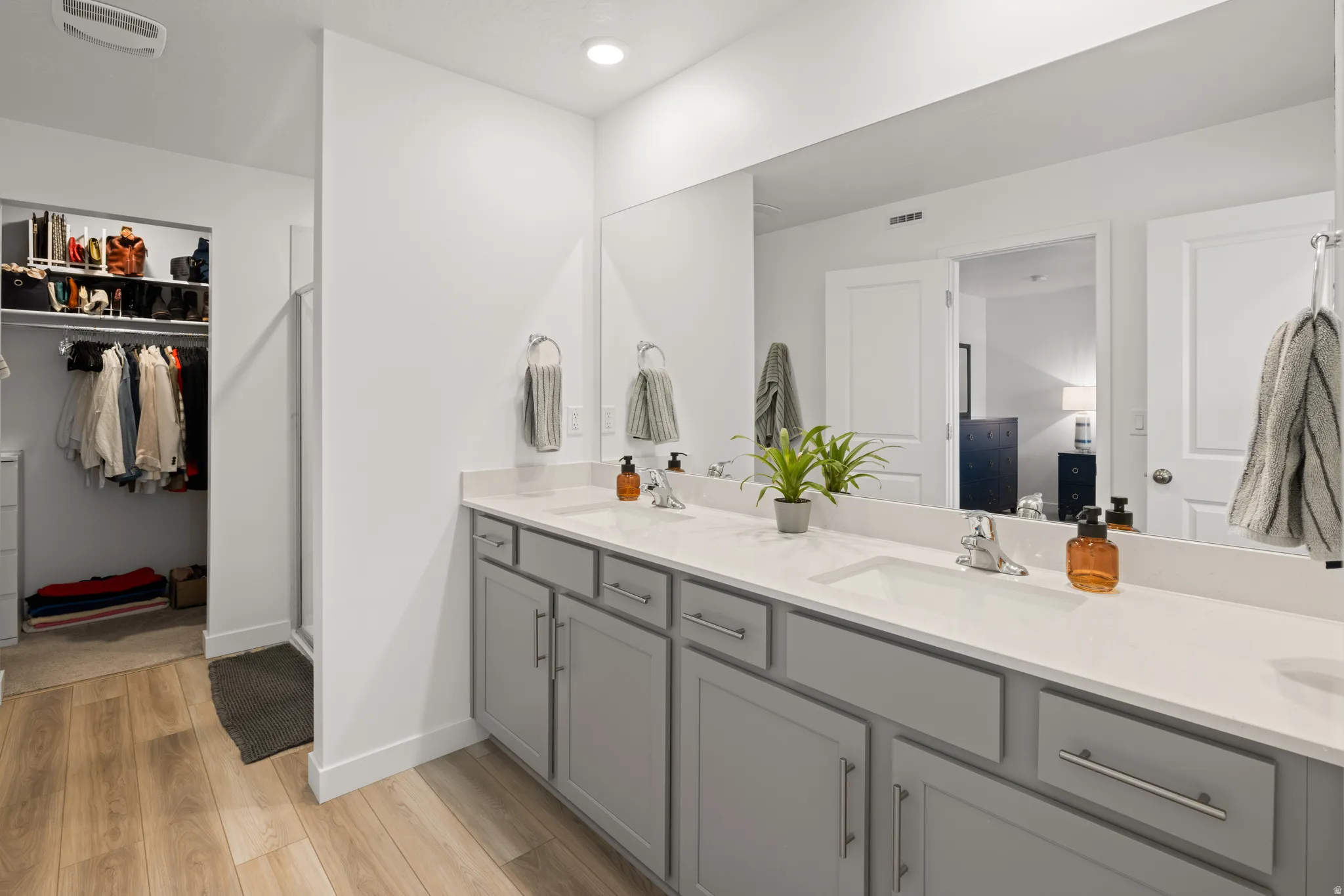 Master bath with gray cabinetry and white countertops, featuring two undermount sinks with chrome faucets, a full-width mirror, and overhead recessed lighting