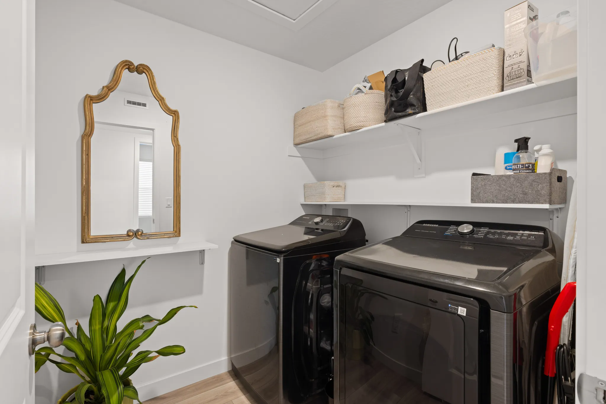 Dedicated upstairs laundry area featuring a washer and dryer, wood-finish flooring, white walls, and built-in shelving for storage