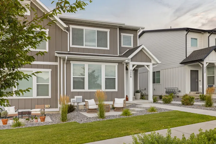 Contemporary townhome exterior featuring a welcoming covered entry, a manicured lawn, and a stone-accented front patio with stepping stones