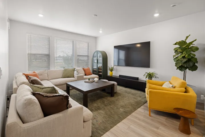Spacious living area featuring light wood-finish flooring, recessed lighting, and large windows with blinds