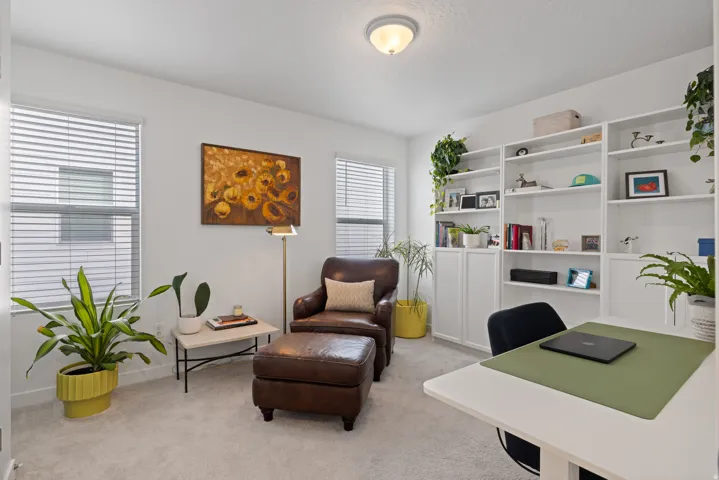 Bedroom 2 being used as a home office, featuring white walls, light carpet flooring, and two windows with horizontal blinds