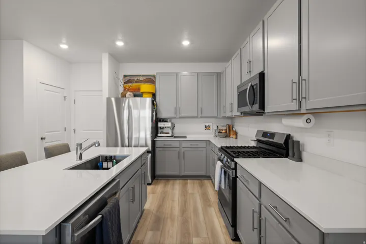 Modern kitchen featuring light gray cabinetry, stainless steel appliances, light-toned countertops, and wood-finish flooring