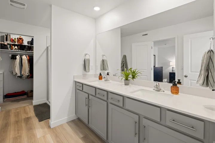 Master bath with gray cabinetry and white countertops, featuring two undermount sinks with chrome faucets, a full-width mirror, and overhead recessed lighting