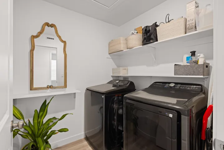 Dedicated upstairs laundry area featuring a washer and dryer, wood-finish flooring, white walls, and built-in shelving for storage