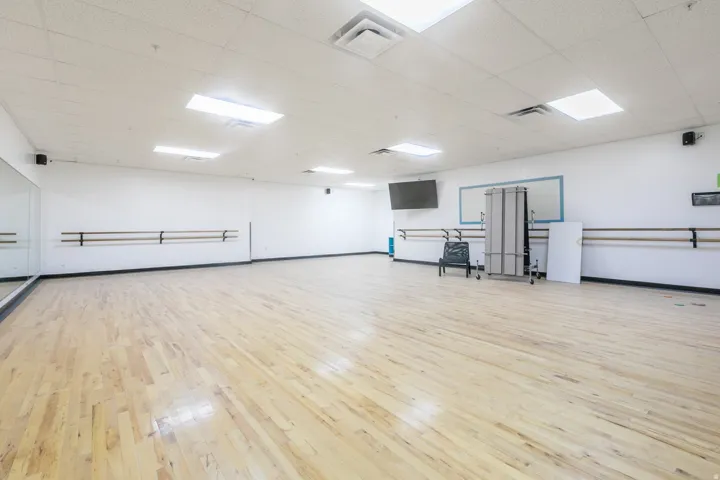 Spacious activity room featuring wood-finish flooring and full-height mirrored wall