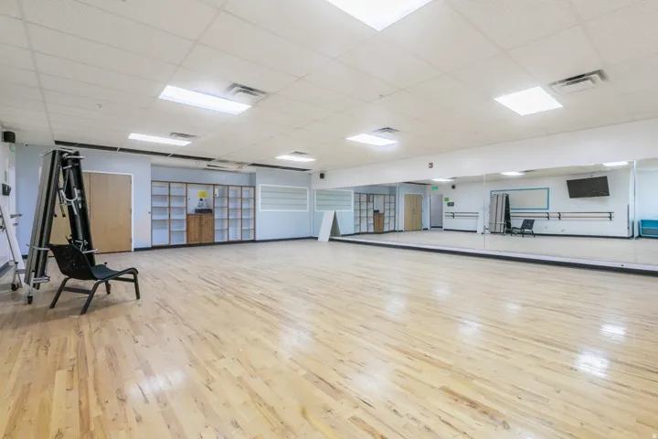 Spacious multi-purpose room featuring wood-finish flooring, full-wall mirrors, recessed lighting, and built-in shelving
