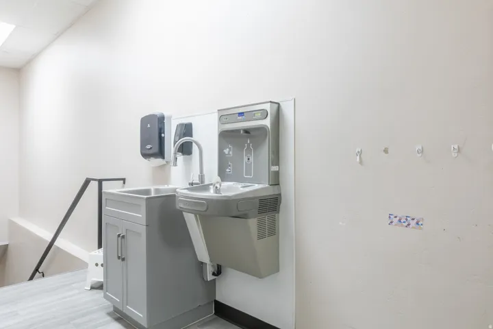 Utility sink with gray shaker-style cabinetry, stainless steel faucet, and built-in water bottle filling station