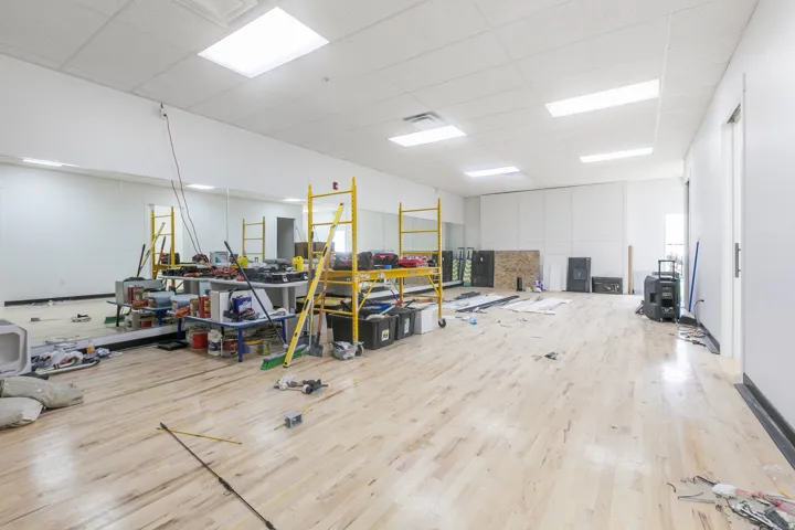 Spacious commercial interior featuring light wood-finish flooring, drop ceiling with integrated rectangular lighting, and expansive wall-mounted mirrors