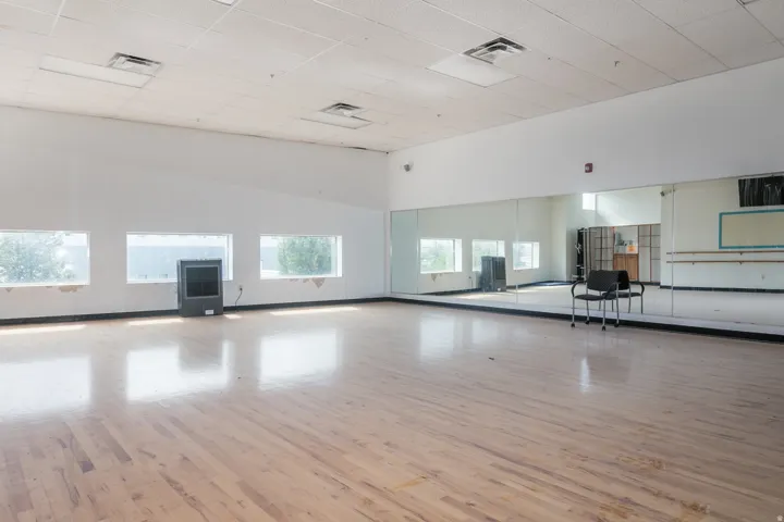 Spacious room featuring wood-finish flooring, a wall of reflective mirrors, and multiple horizontal windows