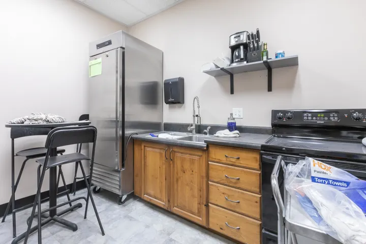 Stainless steel commercial refrigerator, black electric range, wood-finish cabinetry, stainless steel sink with chrome faucet, and gray countertop