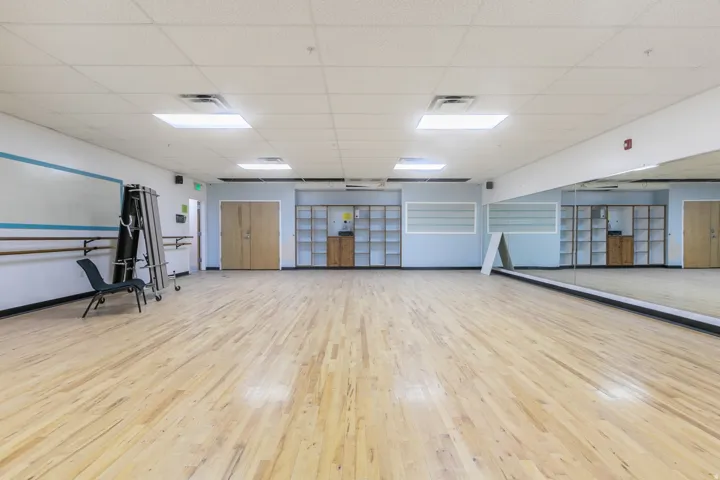 Spacious studio featuring wood-finish flooring, full-wall mirrors, recessed lighting, and wall-mounted barre