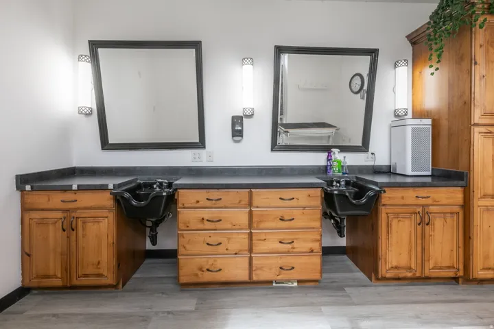 Dual shampoo stations featuring black basins, stone-look countertops, and amber-toned wood cabinetry