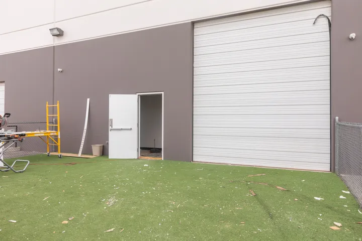 Exterior wall featuring a large roll-up door, a single pedestrian door, and a synthetic turf ground cover
