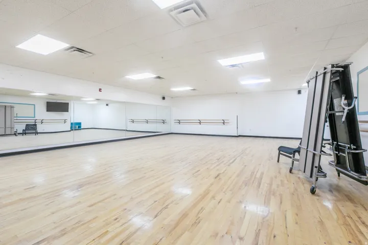 Spacious multipurpose room featuring wood-finish flooring, extensive wall-mounted mirrors, and integrated ballet barres