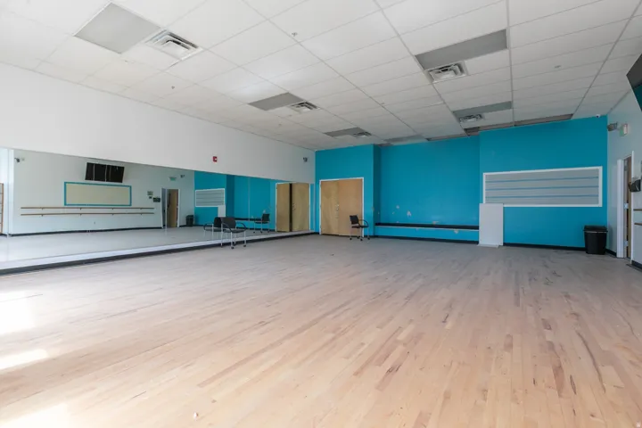 Expansive commercial space featuring light wood-finish flooring, full-length wall mirrors, and a drop ceiling with recessed lighting