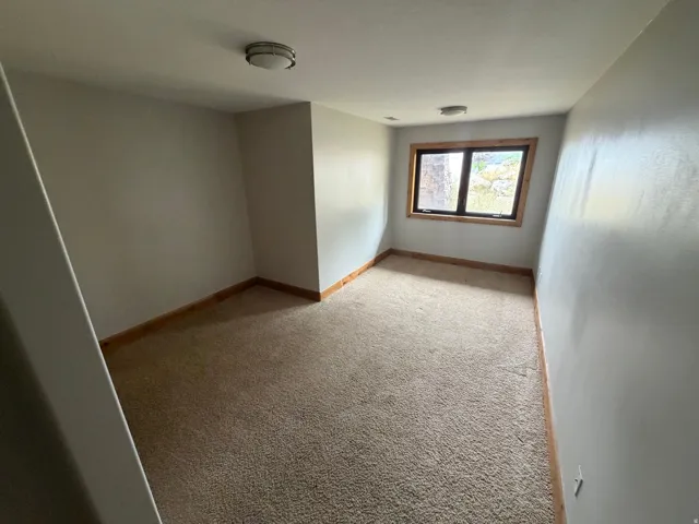 Carpeted room with a single window featuring natural wood trim
