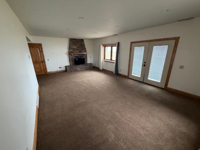 Spacious room with plush brown carpeting, a stone-clad fireplace with a wooden mantle, and a built-in television