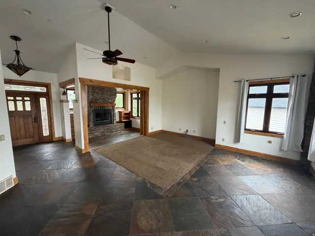 Spacious living area featuring varied flooring, a stone-clad fireplace with a wood mantle, and exposed wood trim