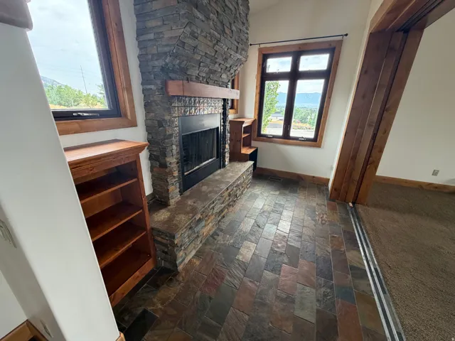 Stone-clad fireplace with a wood mantle, complemented by slate tile flooring and built-in shelving units