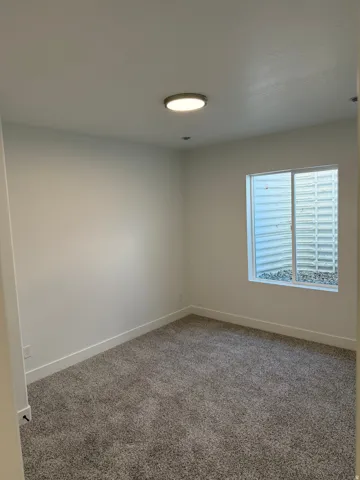 Neutral-toned carpeting grounds this versatile room, featuring a modern flush-mount ceiling light and a window with a window well