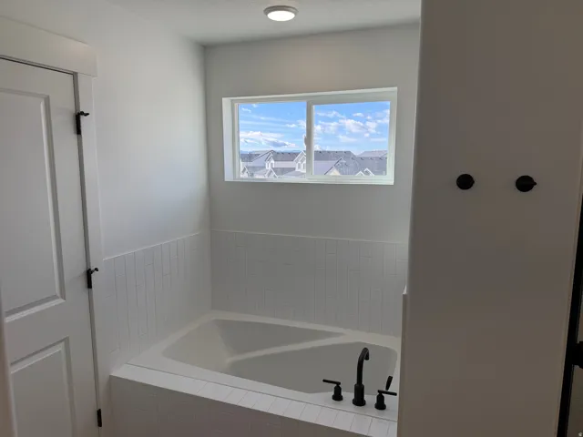 Soaking tub with black matte fixtures, white subway tile surround, and a bright window with neighborhood scenery