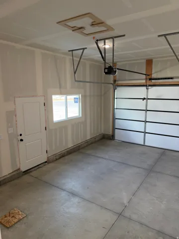 Spacious garage featuring a sectional overhead door with automatic opener, concrete flooring, and a single window for natural light