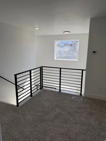 Upper-level landing featuring contemporary black metal horizontal bar railing, neutral-toned carpeting, recessed lighting, and a window with white trim