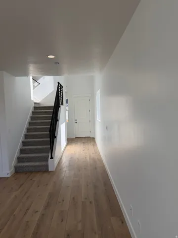 Entryway featuring wood-finish flooring, a carpeted staircase with a black metal railing, white interior doors, and recessed ceiling lighting