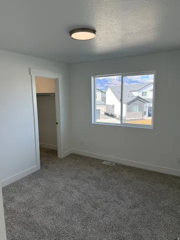 Spacious room featuring neutral carpeting, white trim, a flush-mount ceiling light, and a window overlooking a mountain backdrop
