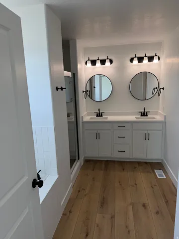 Dual vanity featuring white cabinetry, black hardware, individual round mirrors, and complementary light fixtures