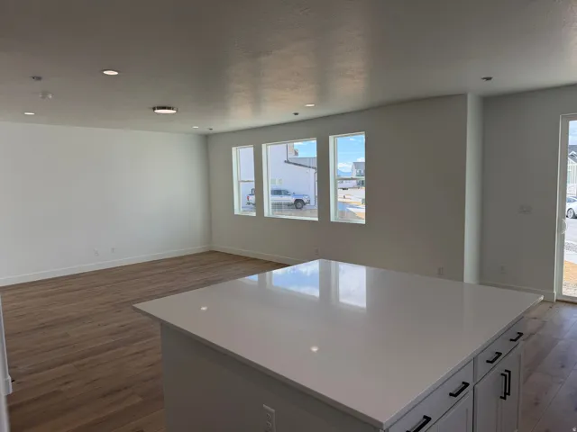 Spacious room featuring a large kitchen island with a light-toned countertop, wood-finish flooring, recessed lighting, and multiple windows