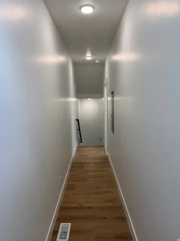 Hallway featuring wood-finish flooring, white baseboards, light grey walls, and recessed ceiling lighting