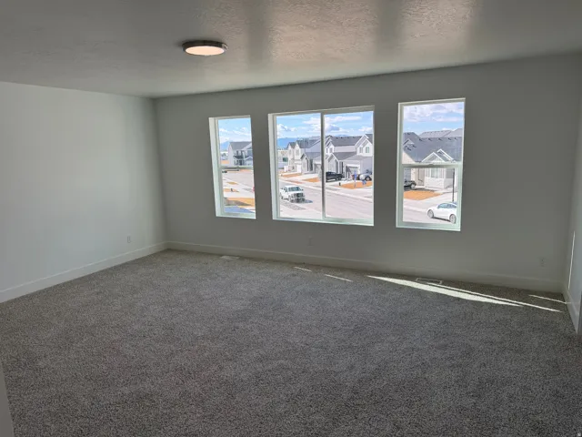 Bright room featuring three large windows, neutral gray carpeting, white painted walls, and a contemporary flush-mount ceiling light fixture