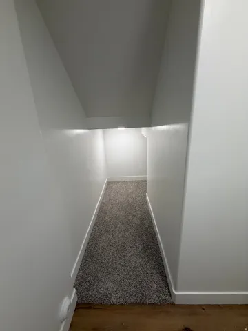 Carpeted hallway with white baseboards and white walls